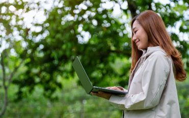 A young asian woman holding and using laptop computer in the outdoors