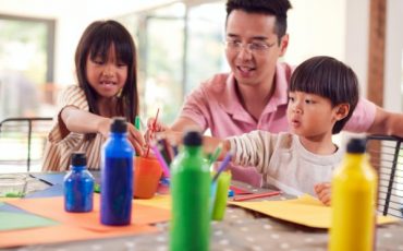 Asian Father With Children Having Fun With Children Doing Craft On Table At Home